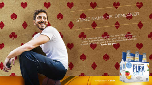 Man smiling next to a six-pack of Pura Still sparkling water with a playful background of red hearts.