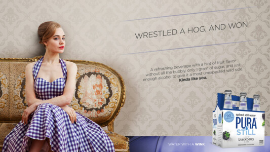 A woman in a checkered dress sits on a vintage sofa next to a promotional ad for Pura Still blackberry drink.