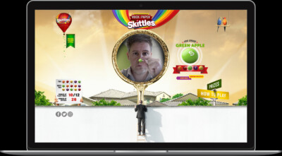 A man in a suit climbs a ladder toward a colorful Skittles game on a computer screen.