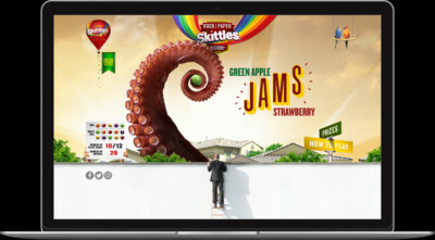 A giant octopus tentacle swirls above buildings in a colorful Skittles advertisement on a laptop screen.